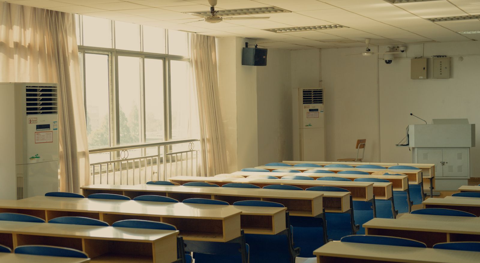 Empty lecture room with rows of desks and chairs lit by natural light